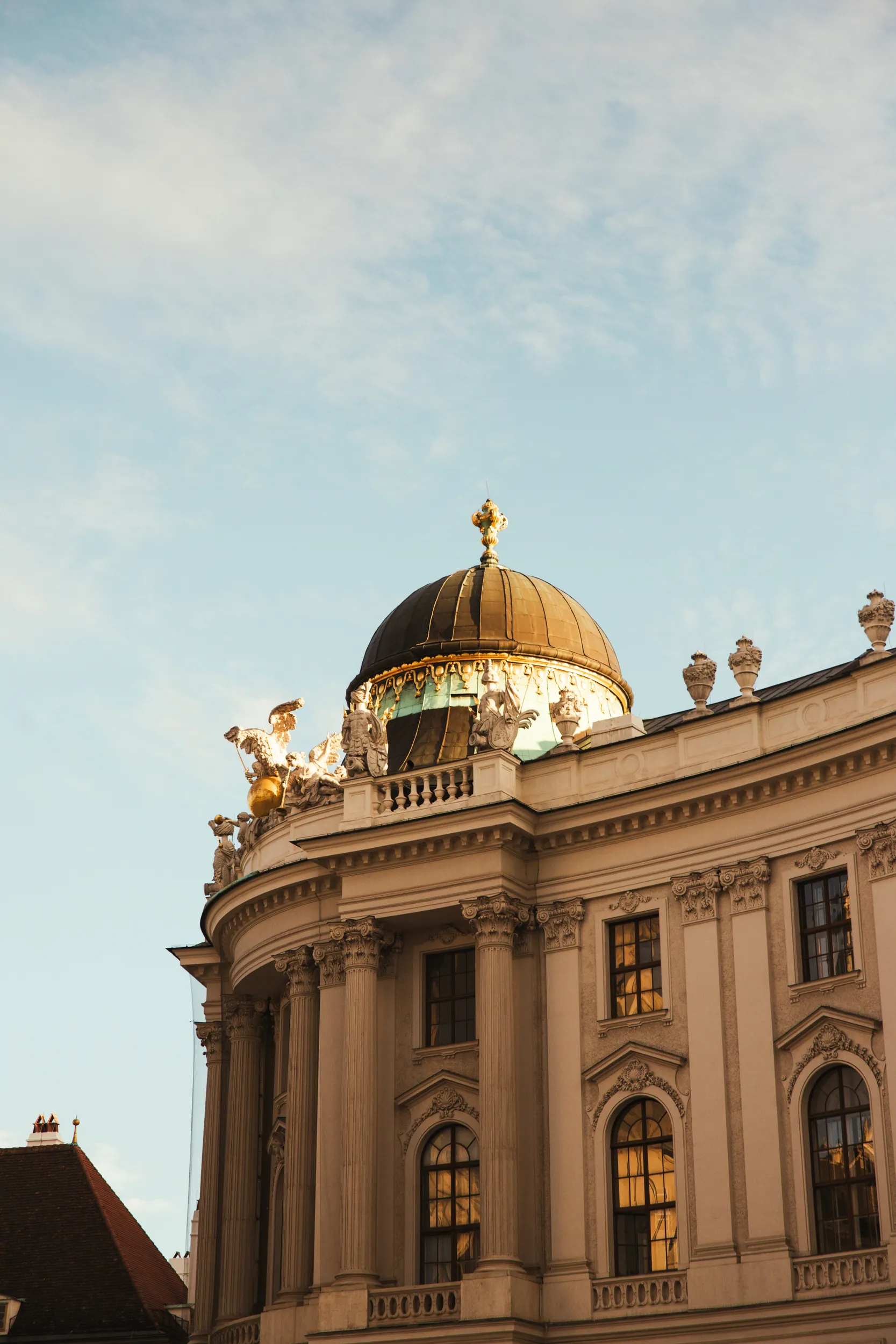 The ornate top of a neoclassical building featuring a dark dome and gilded statues against a pale sky.
